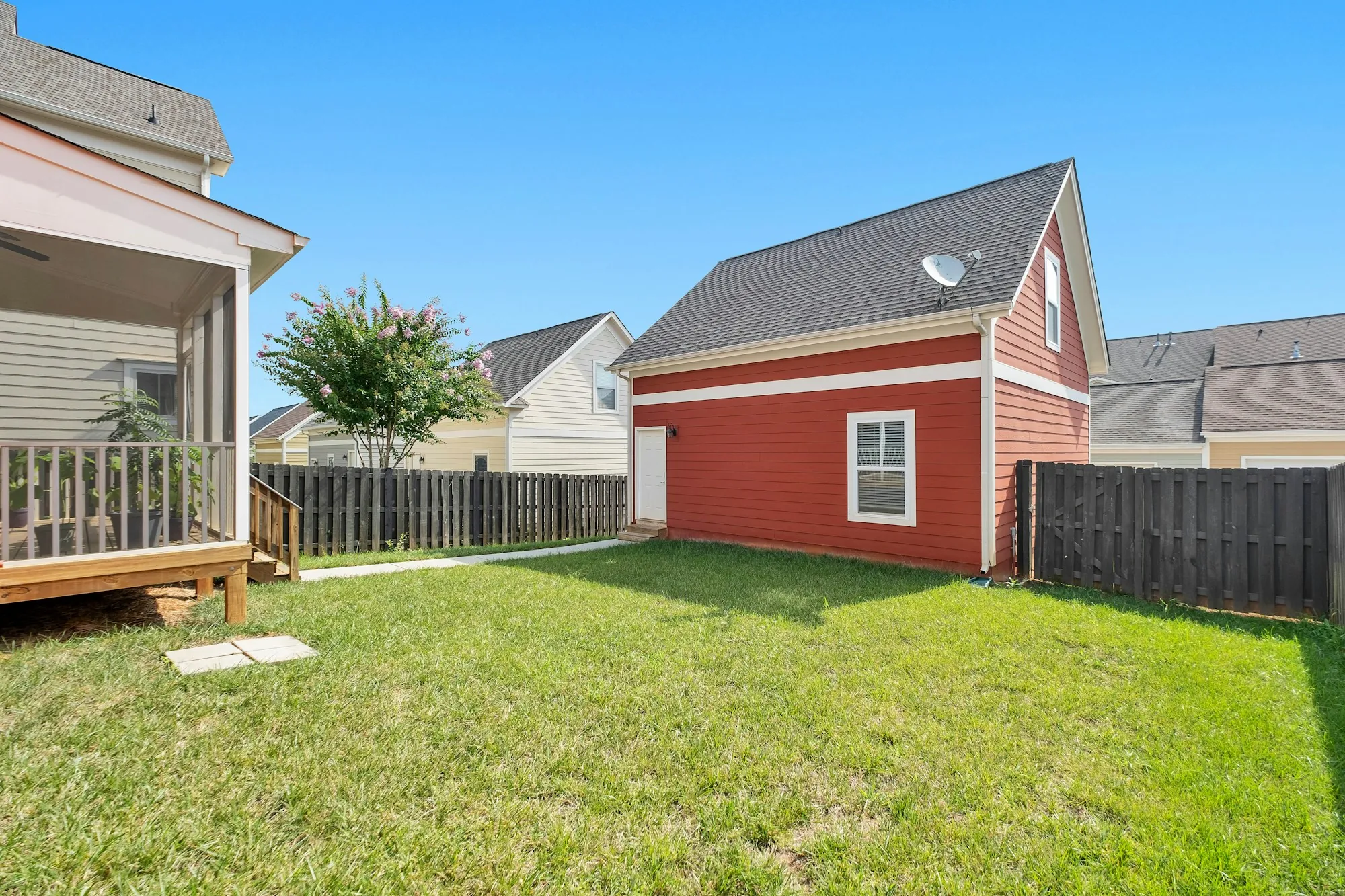Fenced backyard lawn with a wood deck and a red detached garage