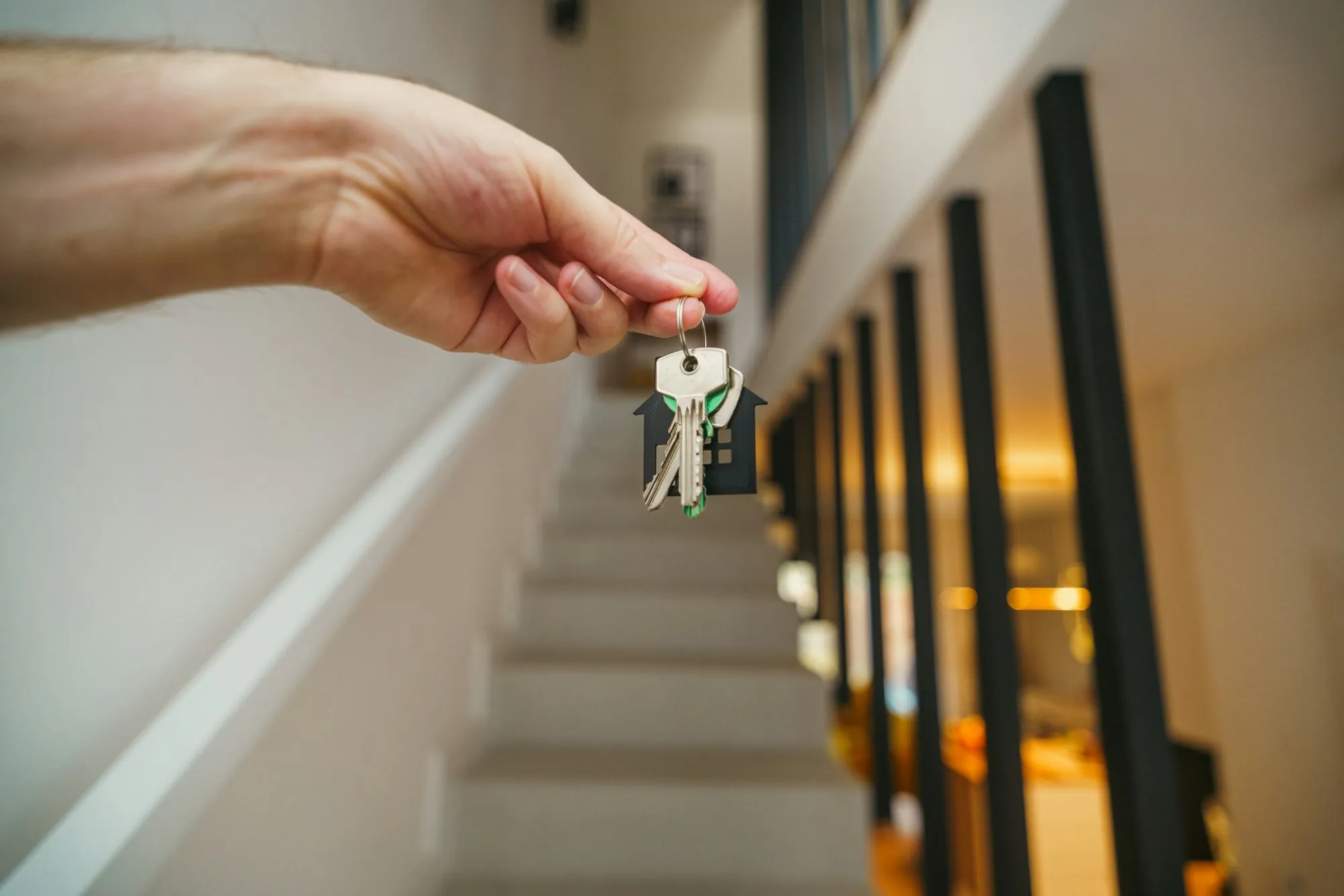 Hand holding a set of keys beside a staircase railing